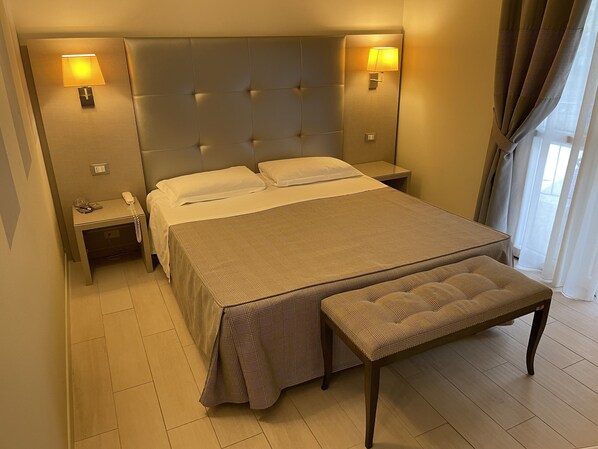 A hotel room with a large bed, two bedside tables, a bedside lamp, a bench, and a view of the outdoors. - Boutique Hotel Calzavecchio (Casalecchio di Reno)