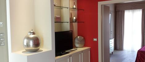 A modern living room with a TV on a white cabinet, a large decorative bowl, and a red accent wall.