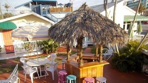 An outdoor seating area with a thatched roof, white plastic chairs, and a wooden bar. - Silver Sands Villas (Fort Myers Beach)