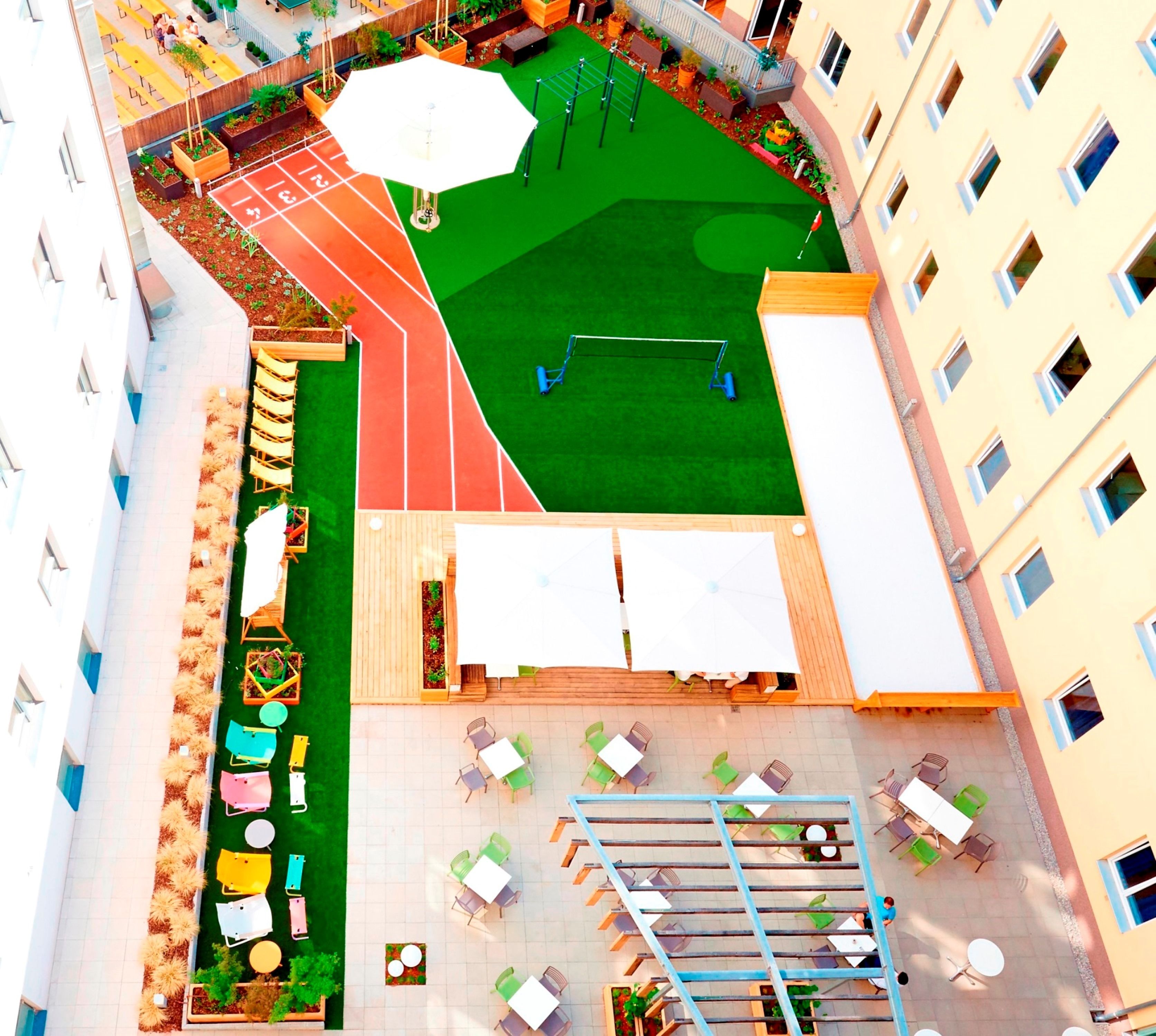 Vista aérea de un patio con pista de atletismo, asientos exteriores y una pequeña zona de jardín.