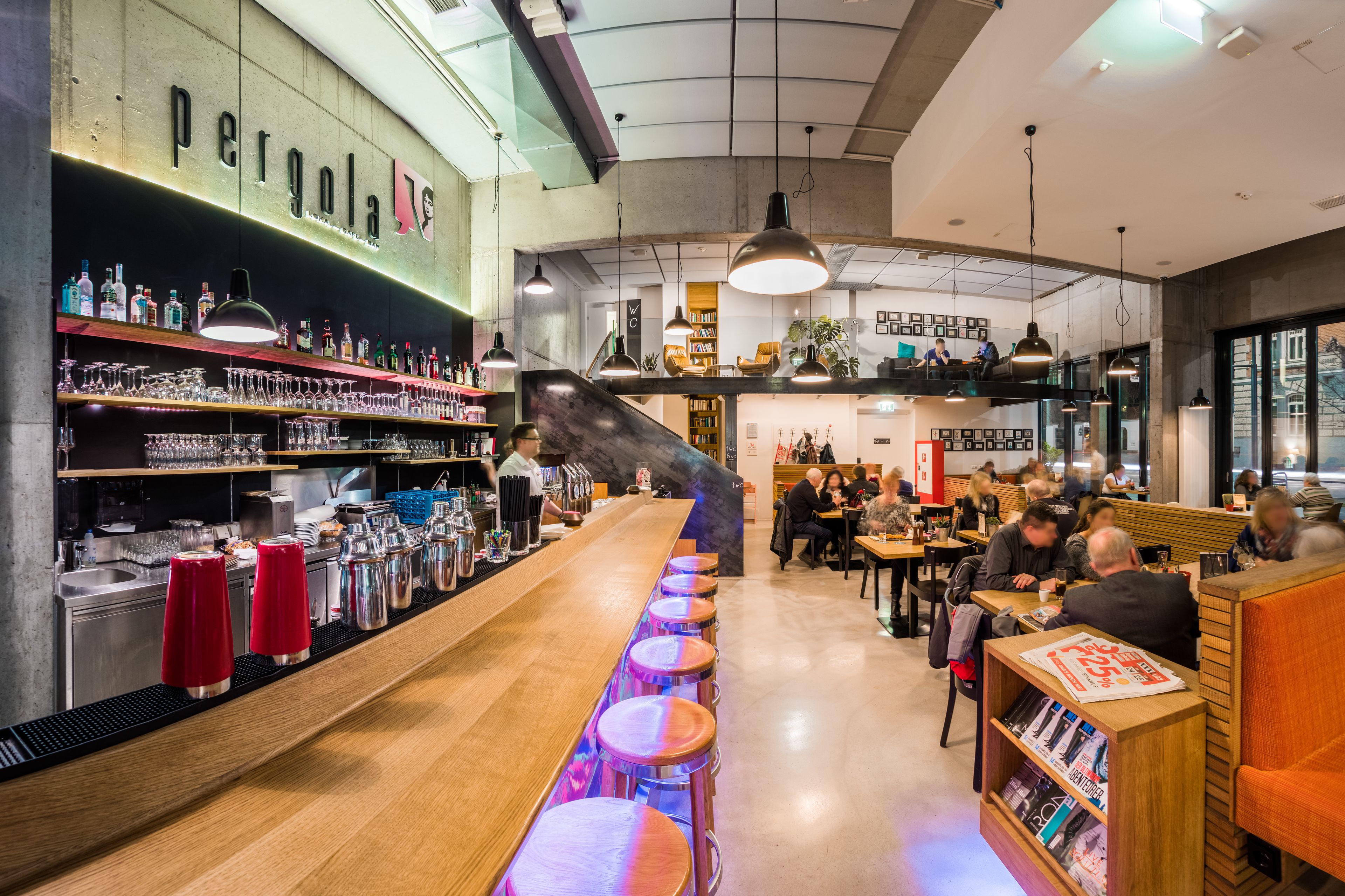 A bar area with stools, a bar counter, and shelves with bottles and glasses.