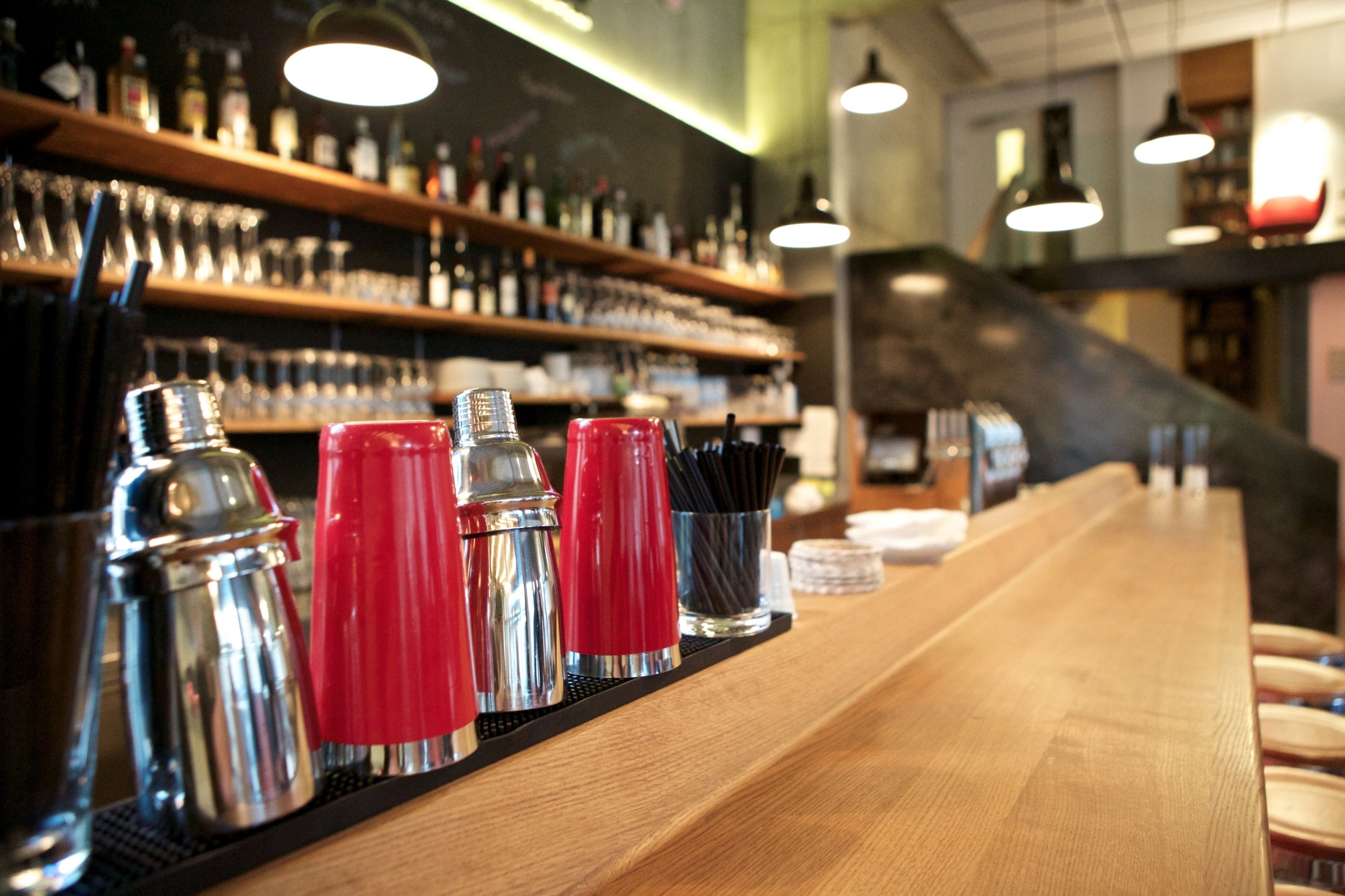 Uma área de bar com balcão de madeira, utensílios de bar e prateleiras com garrafas e copos.