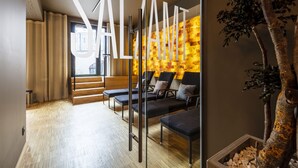 Un interior moderno con una mesa de recepción, una zona de estar con sillas y cojines negros, y una pared con textura.