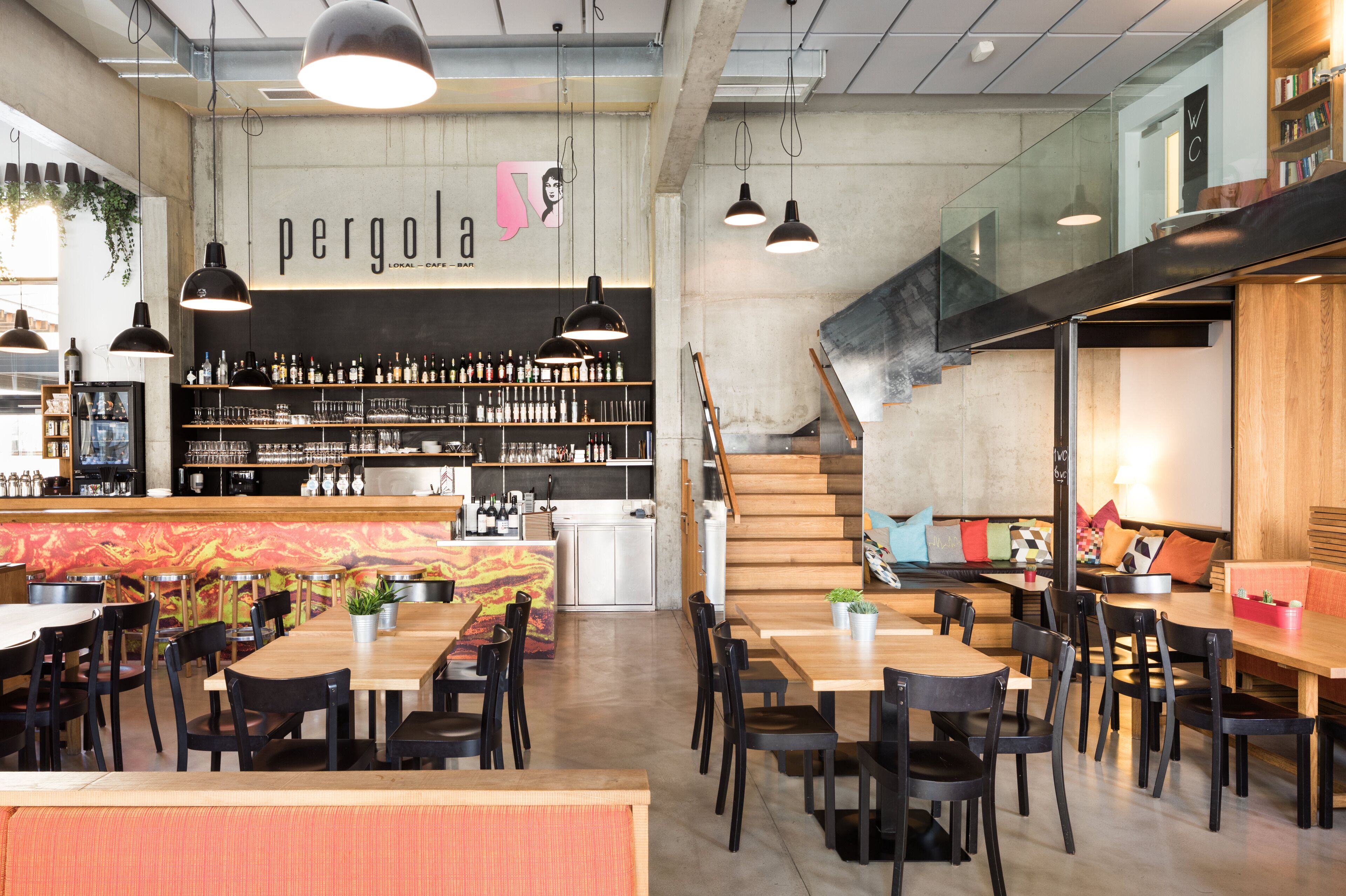 A modern bar area with a visible counter, shelves with bottles, and hanging pendant lights.