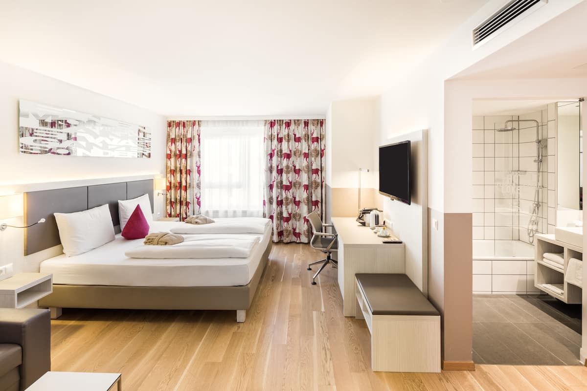 Moderni hotellihuone, jossa on sänky, työpöytä ja suihkutila.