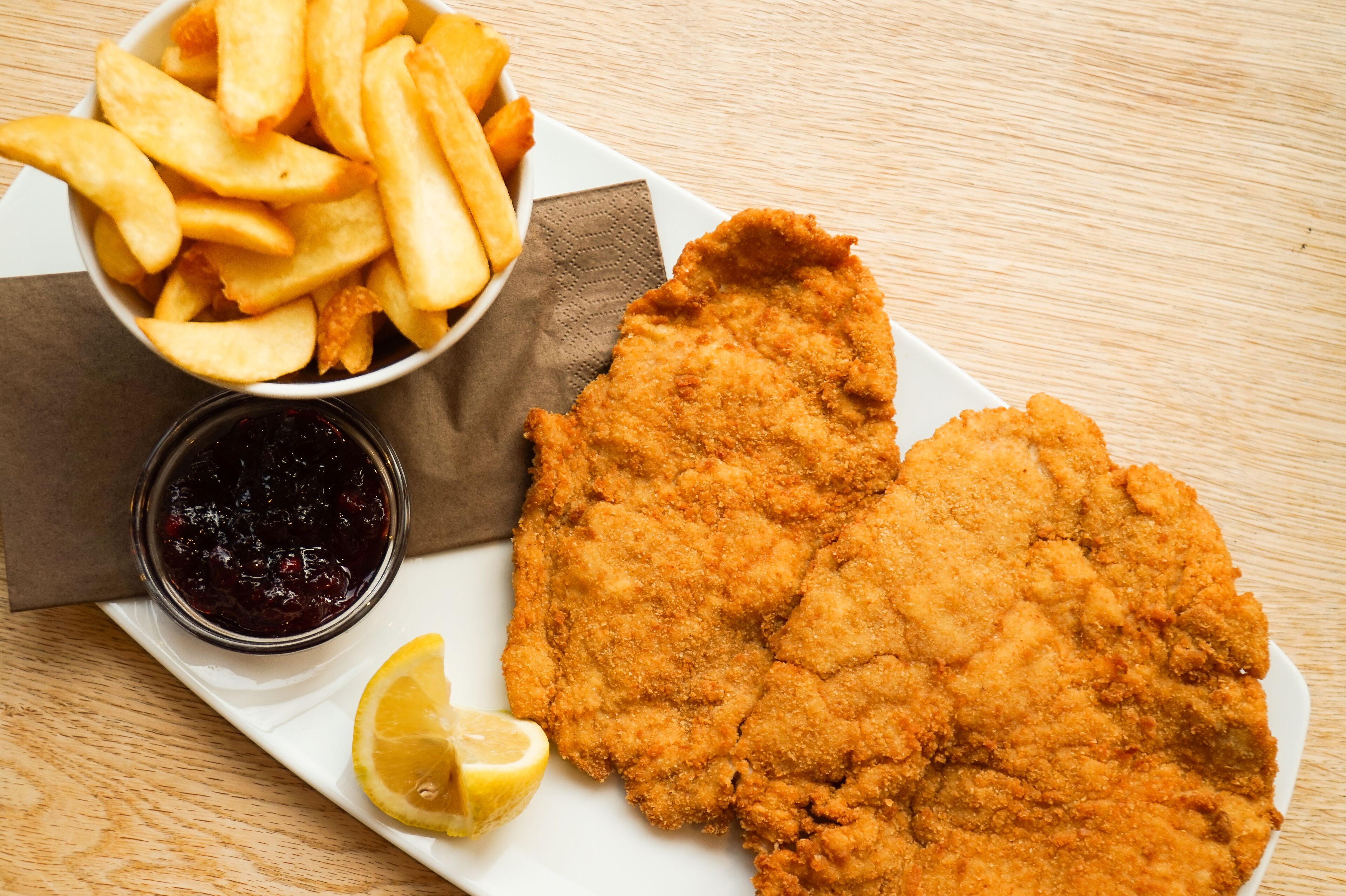 Ein Teller mit einem panierten Schnitzel, Pommes und einer kleinen Soße.