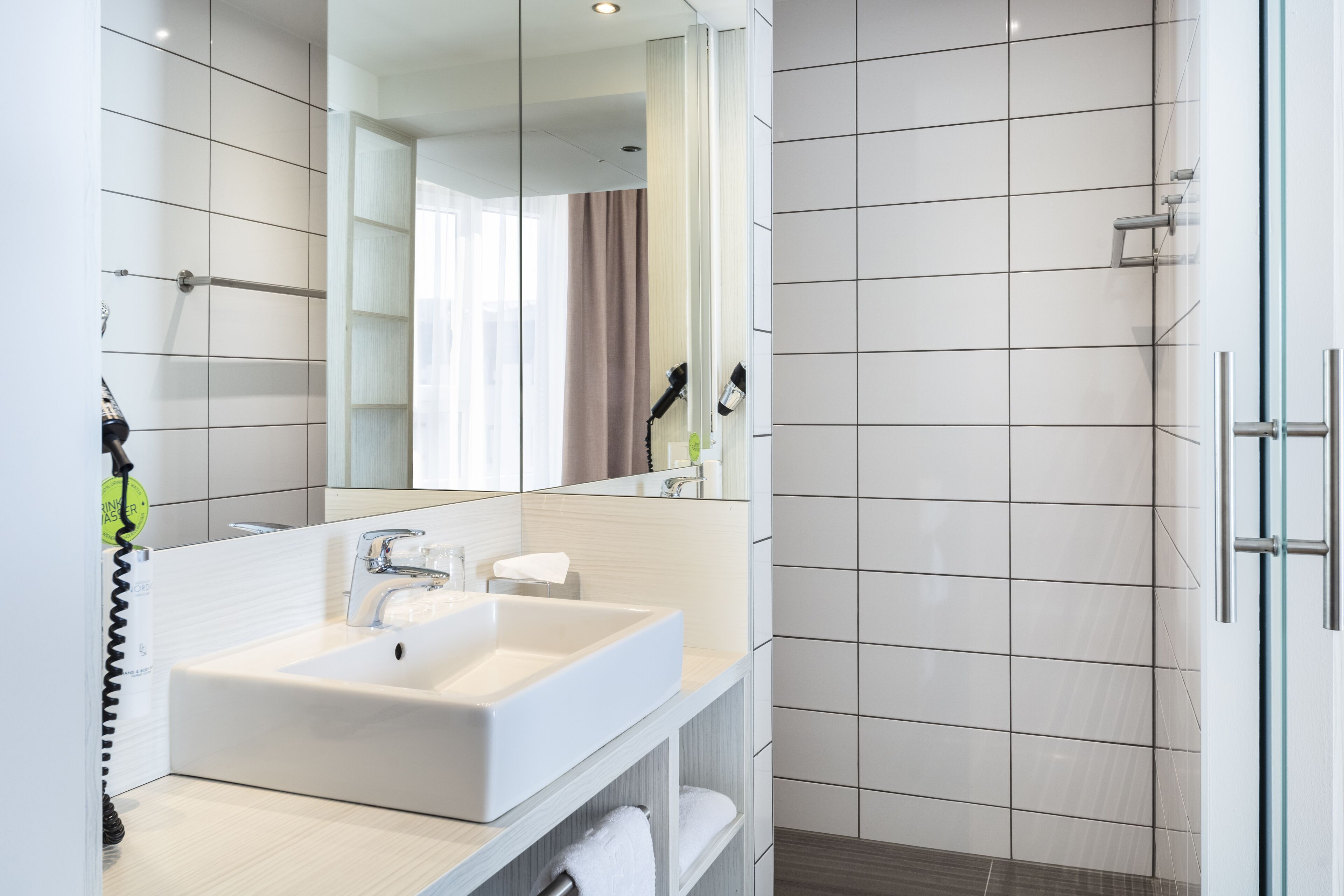 Un baño moderno con un espejo grande, dos lavamanos y una zona de ducha.