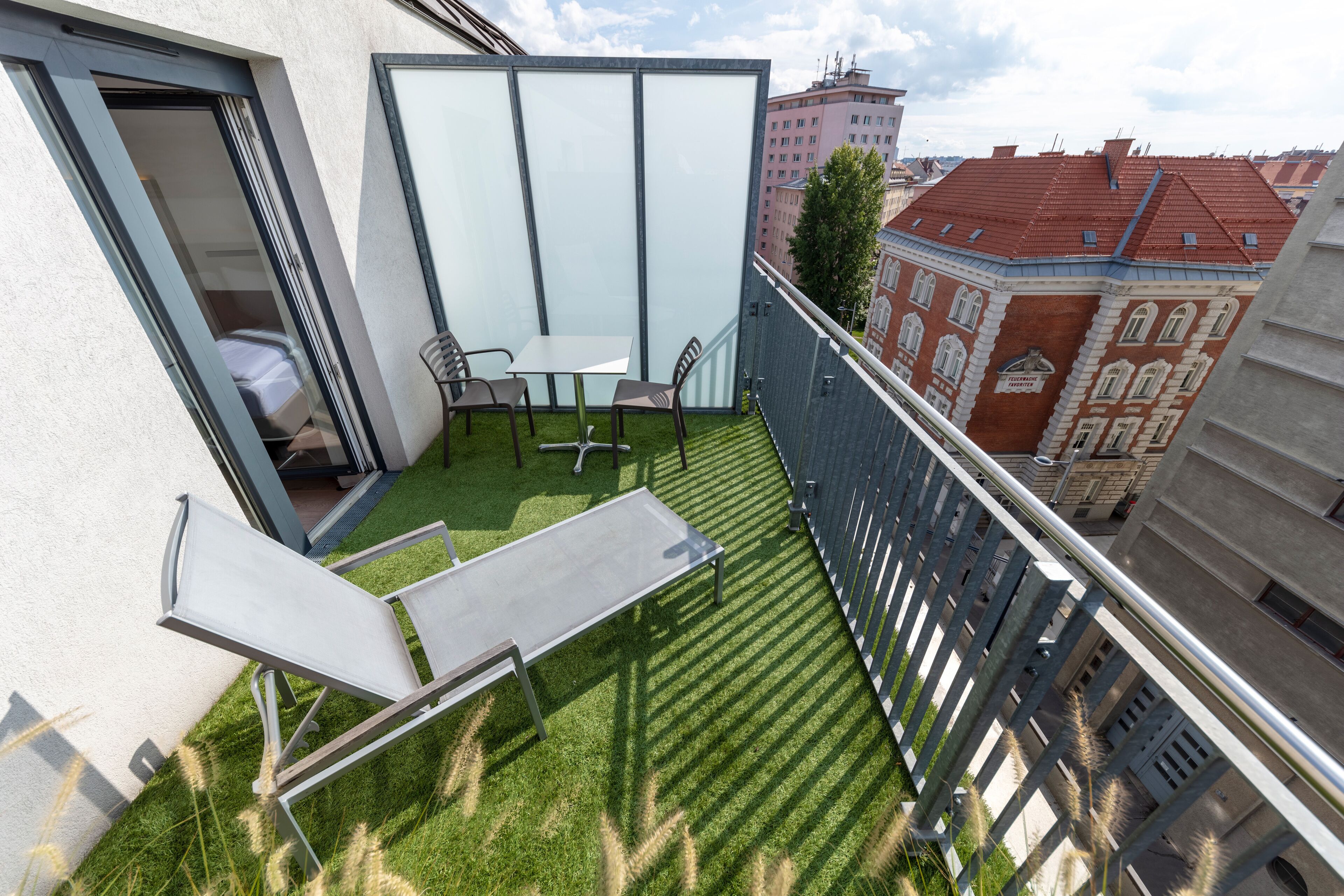 Varanda com mesa e cadeiras, uma pequena área gramada e vista para edifícios ao redor.