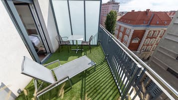 Varanda com mesa e cadeiras, uma pequena área gramada e vista para edifícios ao redor.
