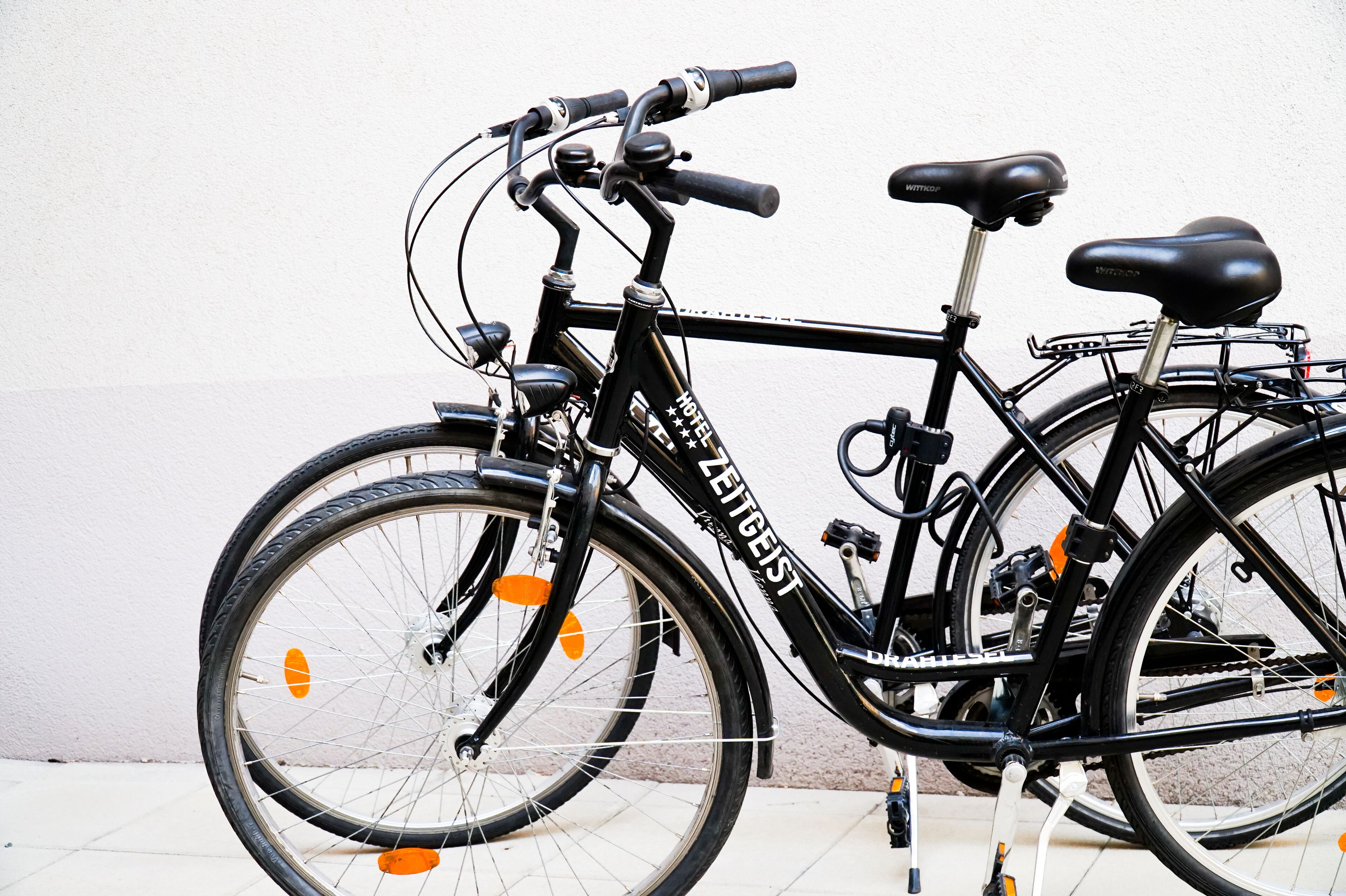 A black bicycle with the brand name "HOTEL ZETTEGIST" on the frame, parked against a white wall.