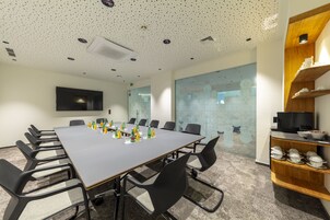 A conference room with a long table, black chairs, a television on the wall, and a glass wall with decorative elements.