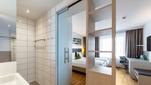 Una habitación de hotel moderna con ducha, cama, escritorio y silla.