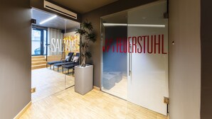 Un espacio de oficina moderno con una puerta de cristal, una planta en maceta y una zona de estar con sillas y una mesa.