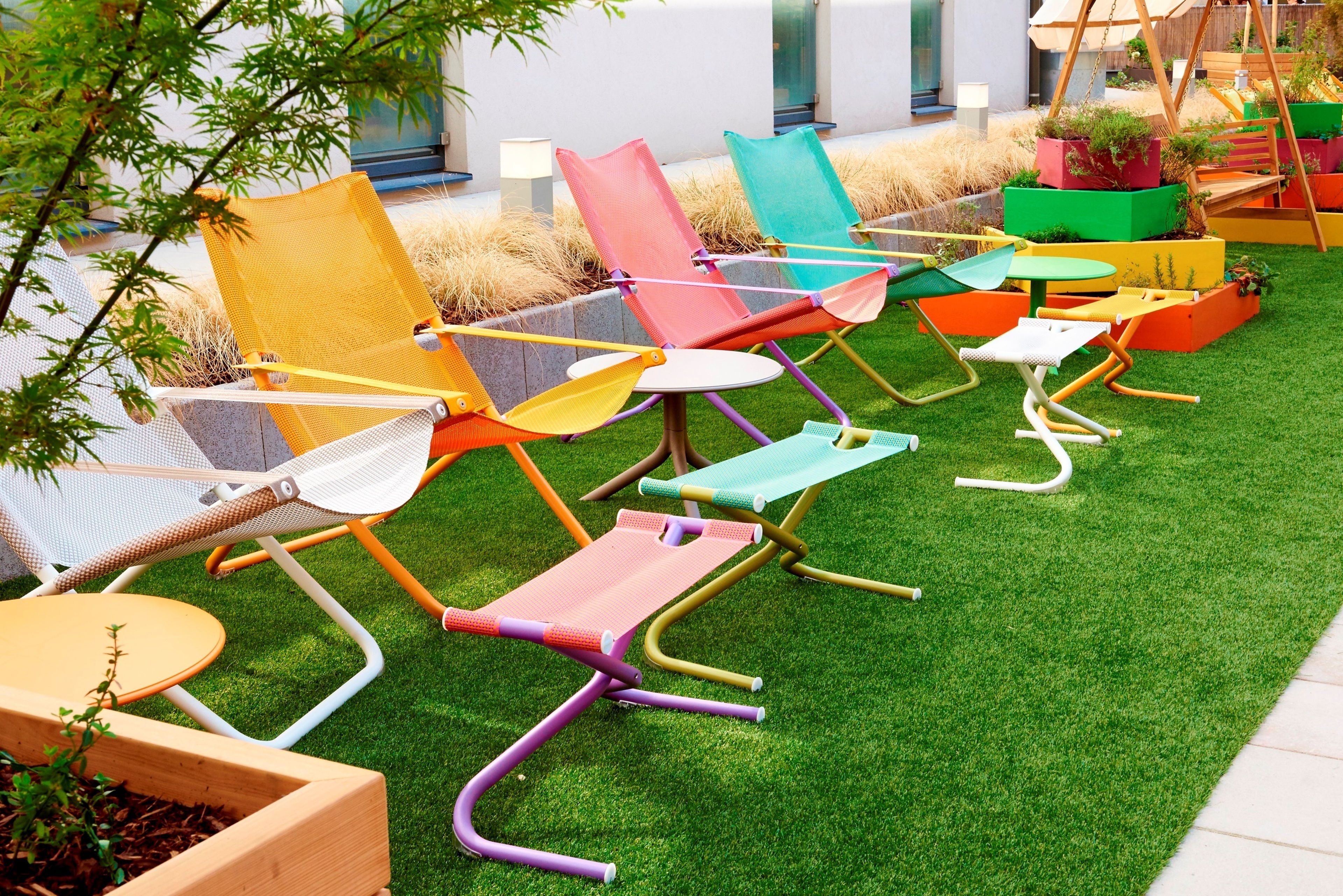 Outdoor seating with colorful chairs and tables, arranged on artificial grass.