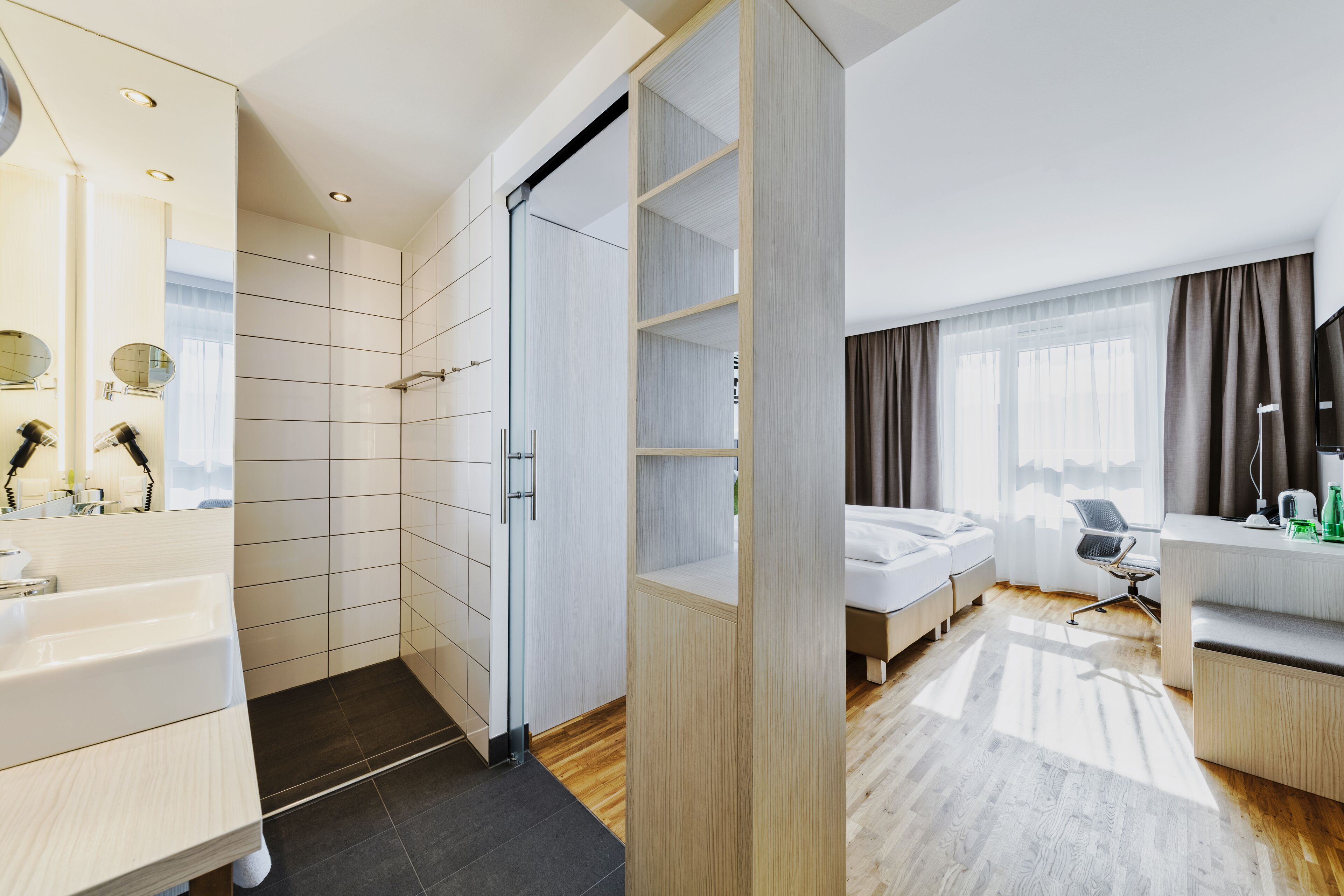 Une chambre d’hôtel moderne dotée d’un grand lit, d’un bureau avec une chaise, d’une salle de bain avec un lavabo et un miroir, et d’une armoire.