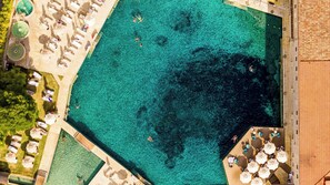 An aerial view of a large, clear blue pool surrounded by sun loungers and umbrellas, with a small pool area and a building adjacent to the pool. - Terme di Saturnia Natural Spa & Golf Resort - The Leading Hotels of the World (Manciano)