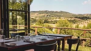 Una mesa de comedor dispuesta con platos, vasos y cubiertos, con vistas a un paisaje pintoresco con colinas y árboles.