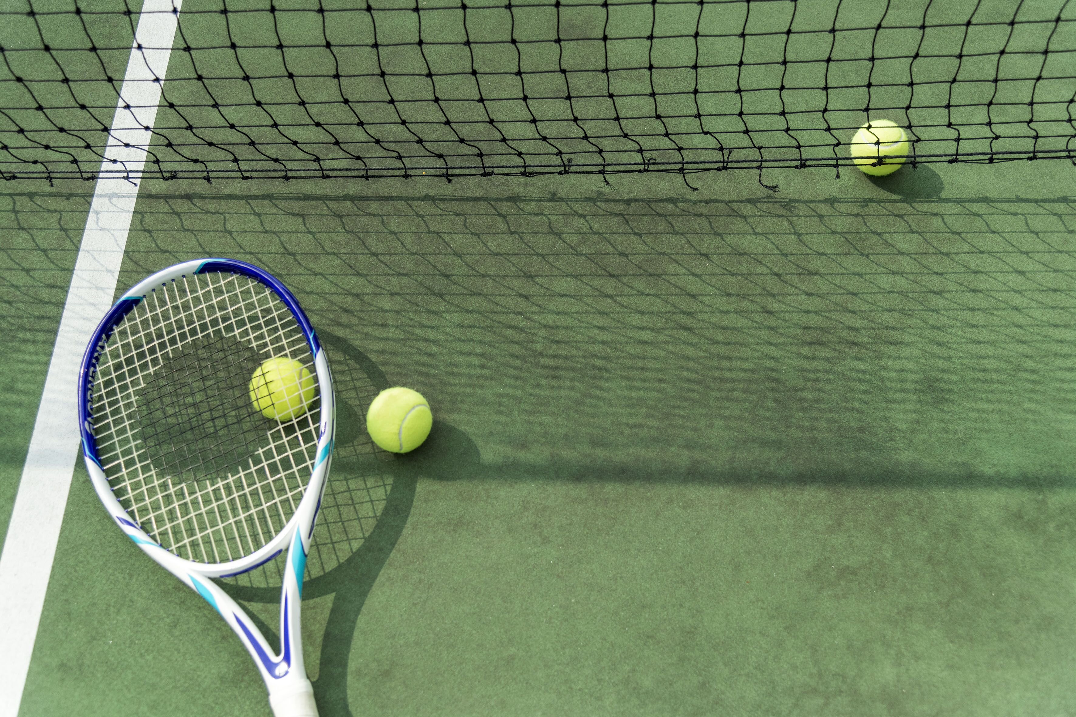 A tennis court with a net, a tennis racket, and two tennis balls.