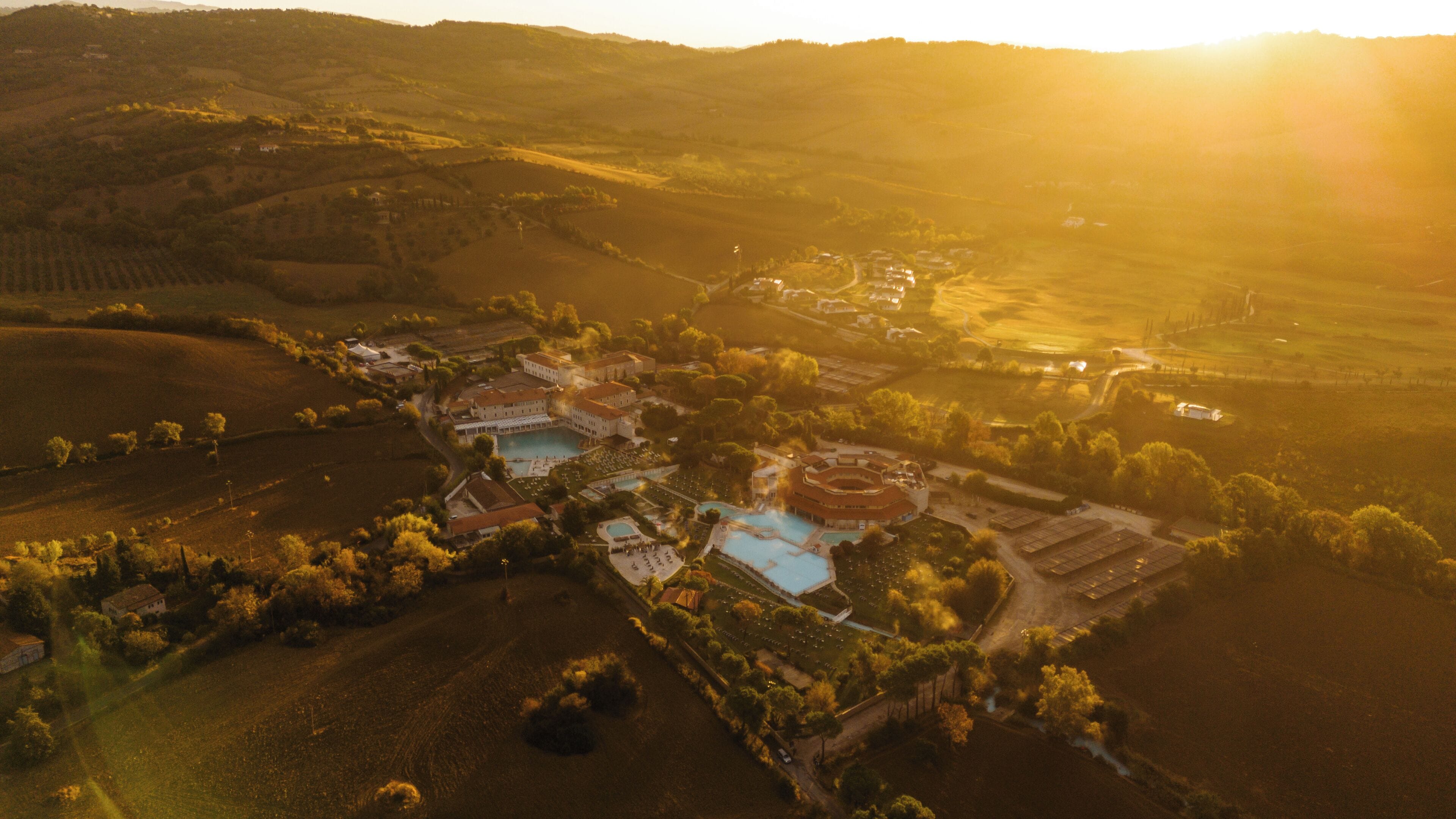 An aerial view of a resort with multiple buildings, a swimming pool, and surrounding fields.