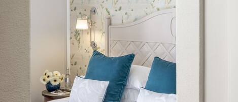 A bedroom with a white headboard, a floral wallpaper, and a blue bedspread.