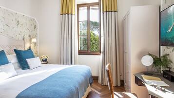 A bedroom with a bed, a desk, a chair, a window with curtains, and a wall-mounted mirror.