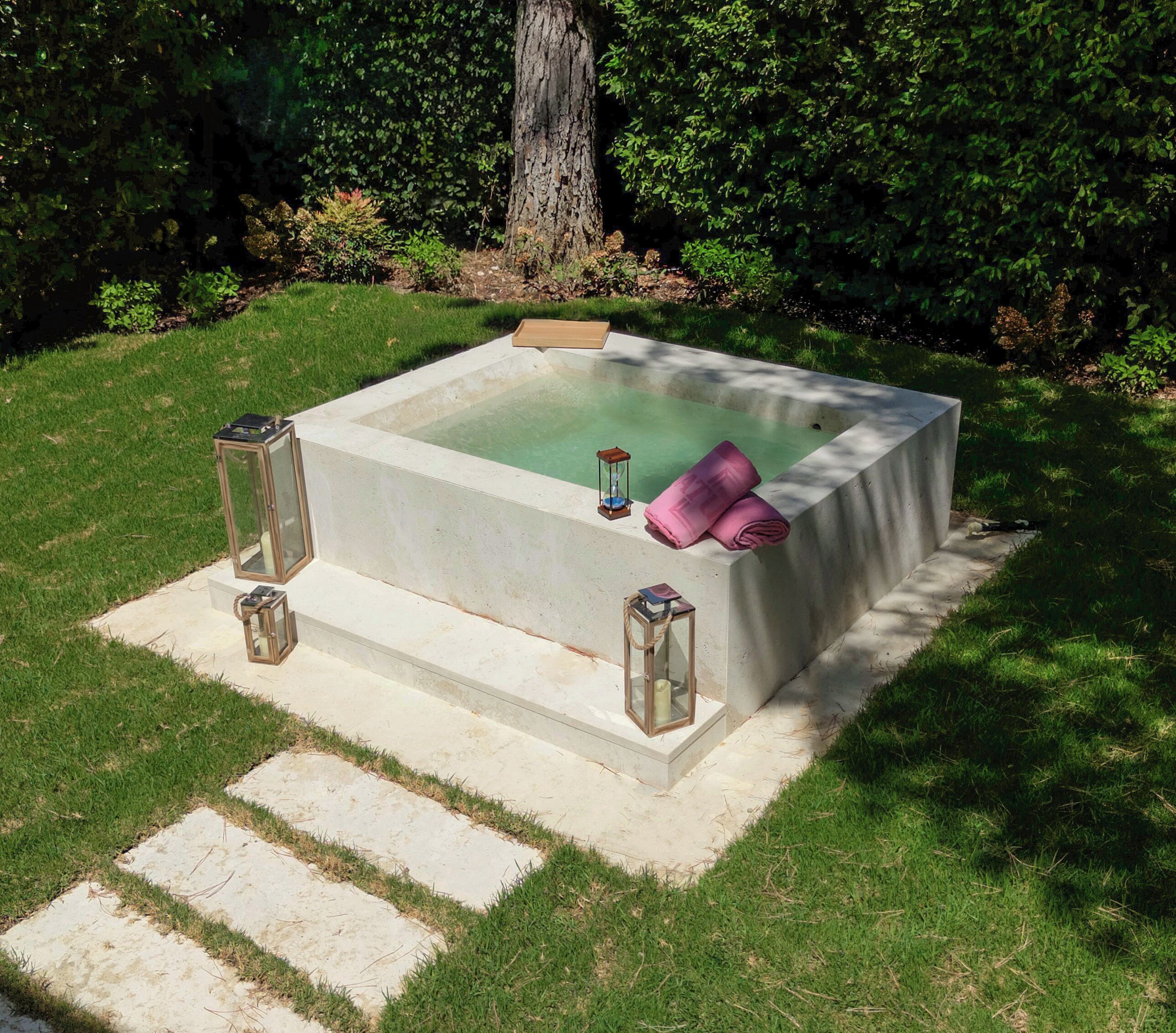 A square hot tub with steps leading up to it, surrounded by grass and trees.