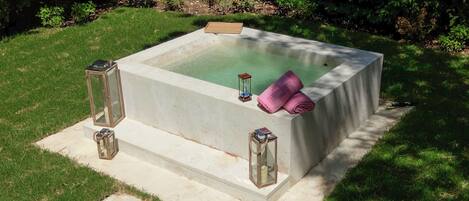 Una bañera de hidromasaje cuadrada con escalones que llevan a ella, rodeada de césped y árboles.