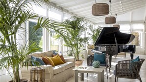 Un salón espacioso con un piano de cola, asientos cómodos y ventanas grandes que dejan entrar luz natural.