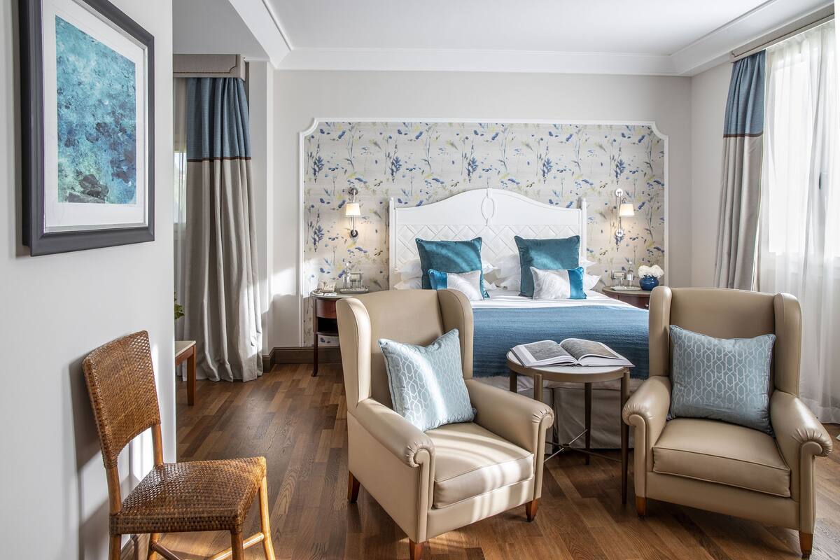 Ein Hotelzimmer mit einem Bett, zwei Sesseln, einem kleinen Tisch und einem Korbstuhl.