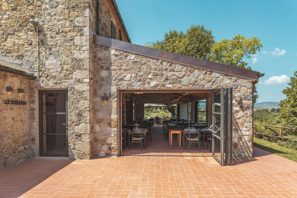Un espacio para comer al aire libre con paredes de piedra y piso de ladrillo, adosado a un edificio con fachada de piedra.