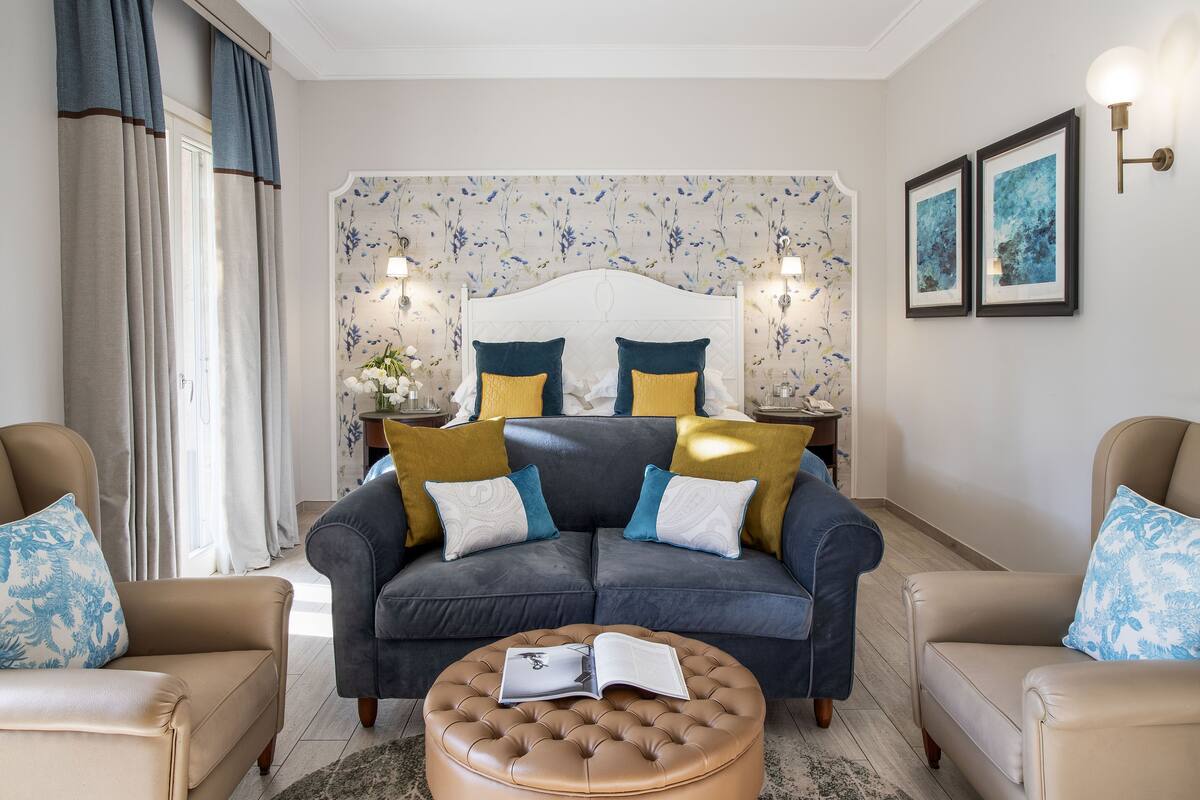 Ein modernes Wohnzimmer mit einem grauen Sofa, zwei Sesseln, einem runden Hocker und einem dekorativen Kopfteil.