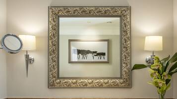 A bathroom with a marble sink, two wall-mounted lamps, a framed artwork, a vase with flowers, and two towels on a shelf.