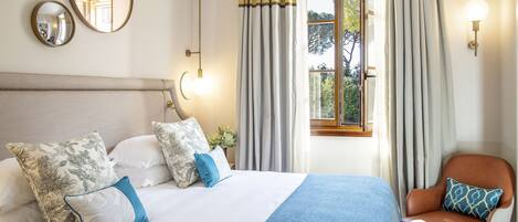 A neatly made bed with a blue blanket, a chair with a patterned cushion, and a window with curtains.