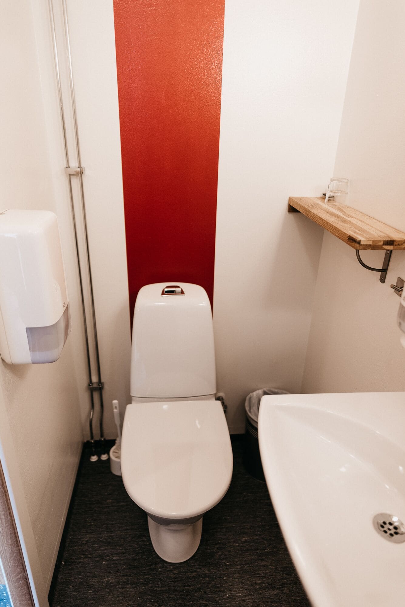 Un baño pequeño con inodoro, lavamanos y una pared de acento rojo.