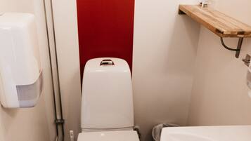 Un baño pequeño con inodoro, lavamanos y una pared de acento rojo.