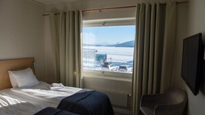 Habitación de hotel con dos camas, una silla y un gran ventanal con cortinas.