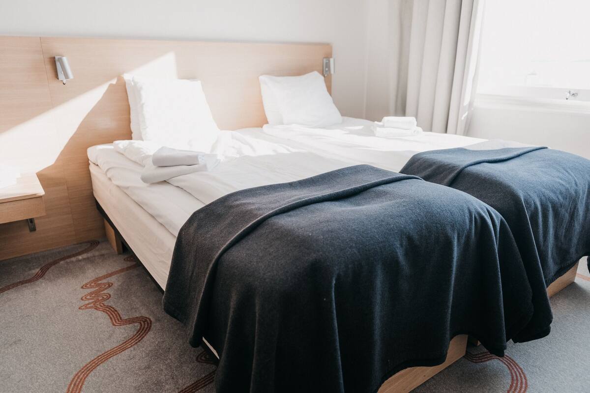 A hotel room with two beds, a wooden headboard, a nightstand, and a window with curtains.