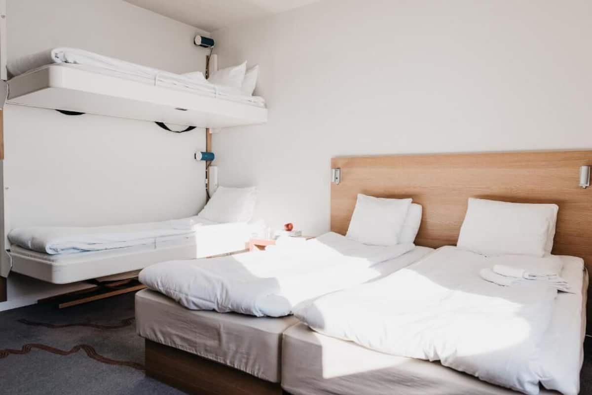 A hotel room with a bunk bed, a single bed, and a wooden headboard.