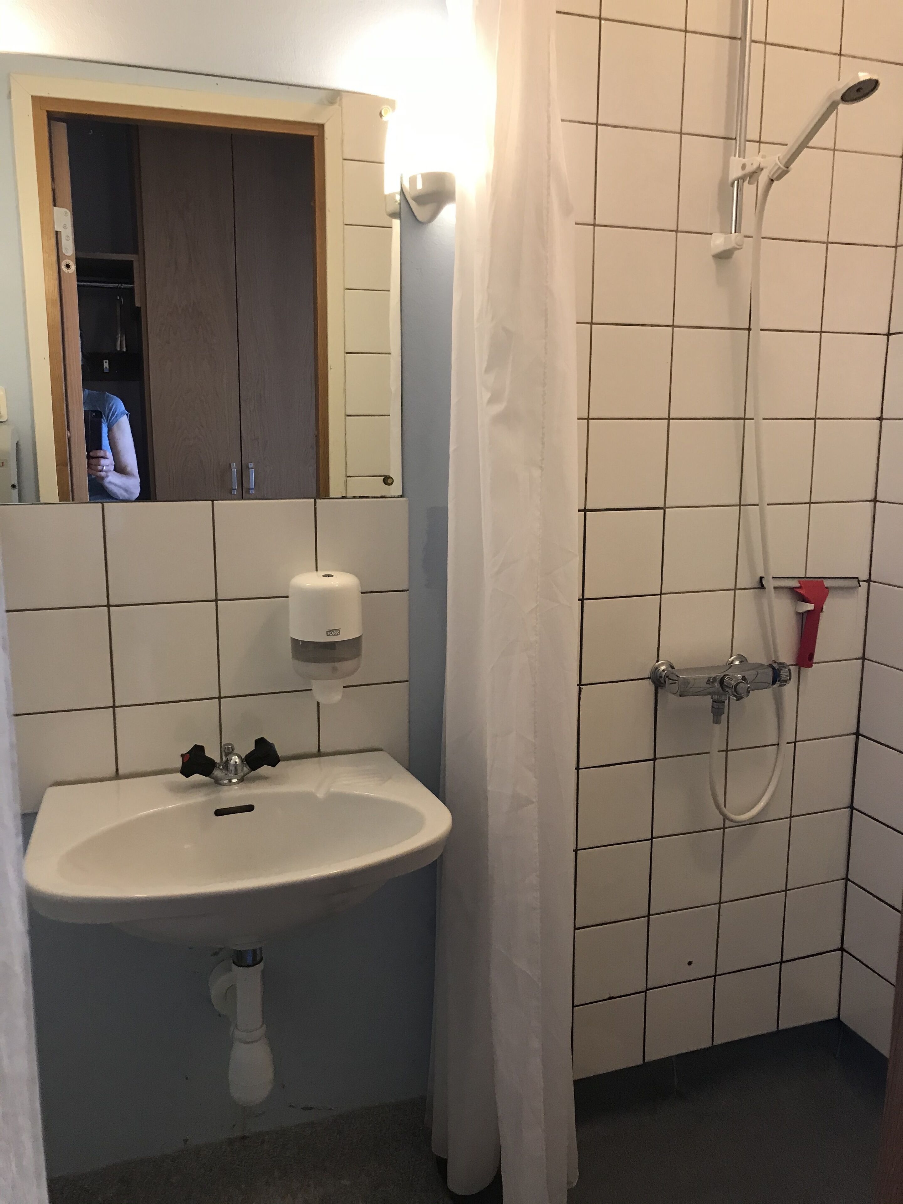 A bathroom with a sink, a mirror, a shower, and a door.