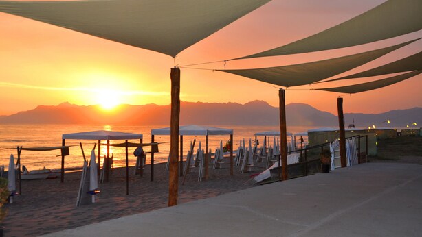 A beach with sun umbrellas and tables, a clear sky, and mountains in the background. - Riviera Spineta (Battipaglia)