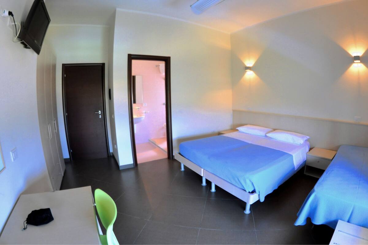 A hotel room with a bed, bedside tables, a desk with a chair, and a TV mounted on the wall.