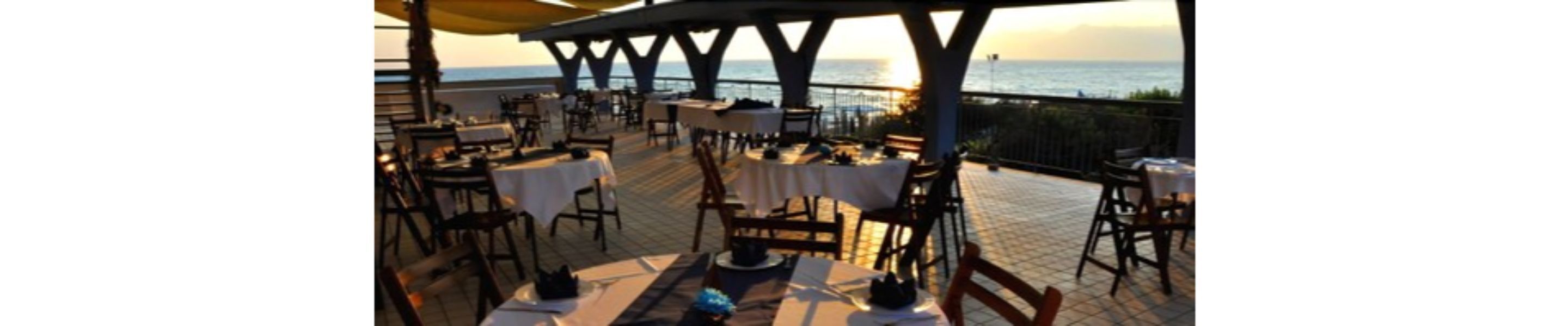 An outdoor dining area with tables and chairs, overlooking the sea.