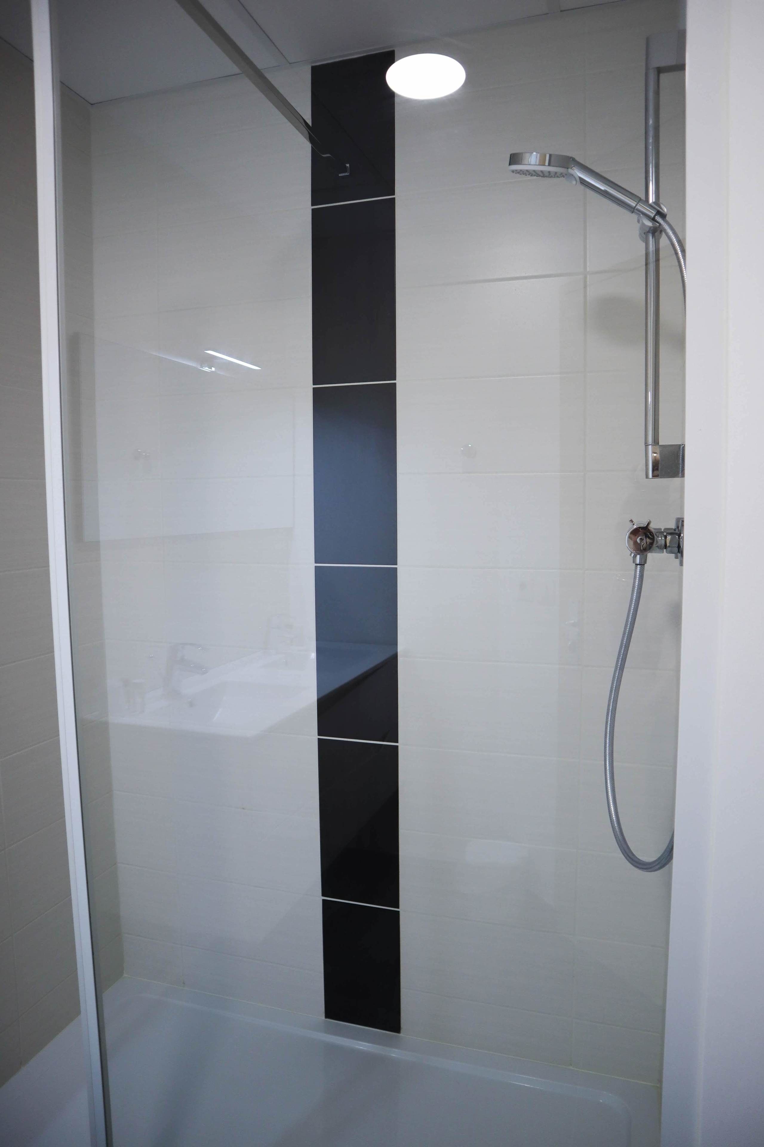 Un box de ducha moderno con puerta de vidrio, un cabezal de ducha manual y un grifo empotrado.