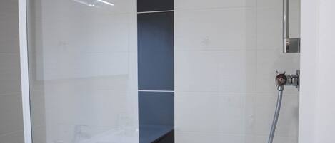 Un box de ducha moderno con puerta de vidrio, un cabezal de ducha manual y un grifo empotrado.