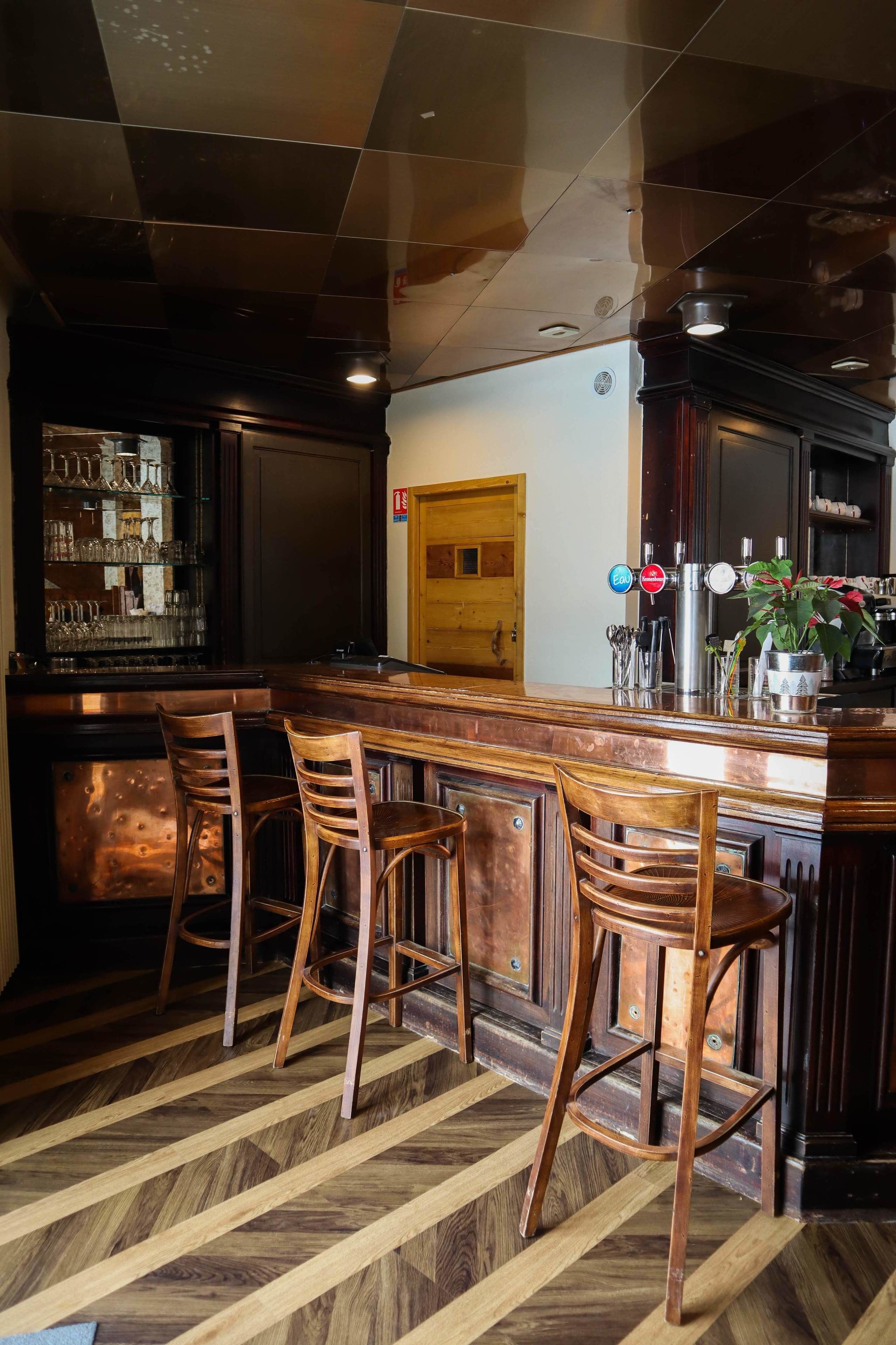 Una zona de bar con taburetes de madera, una barra con vitrina de vidrio y una puerta al fondo.
