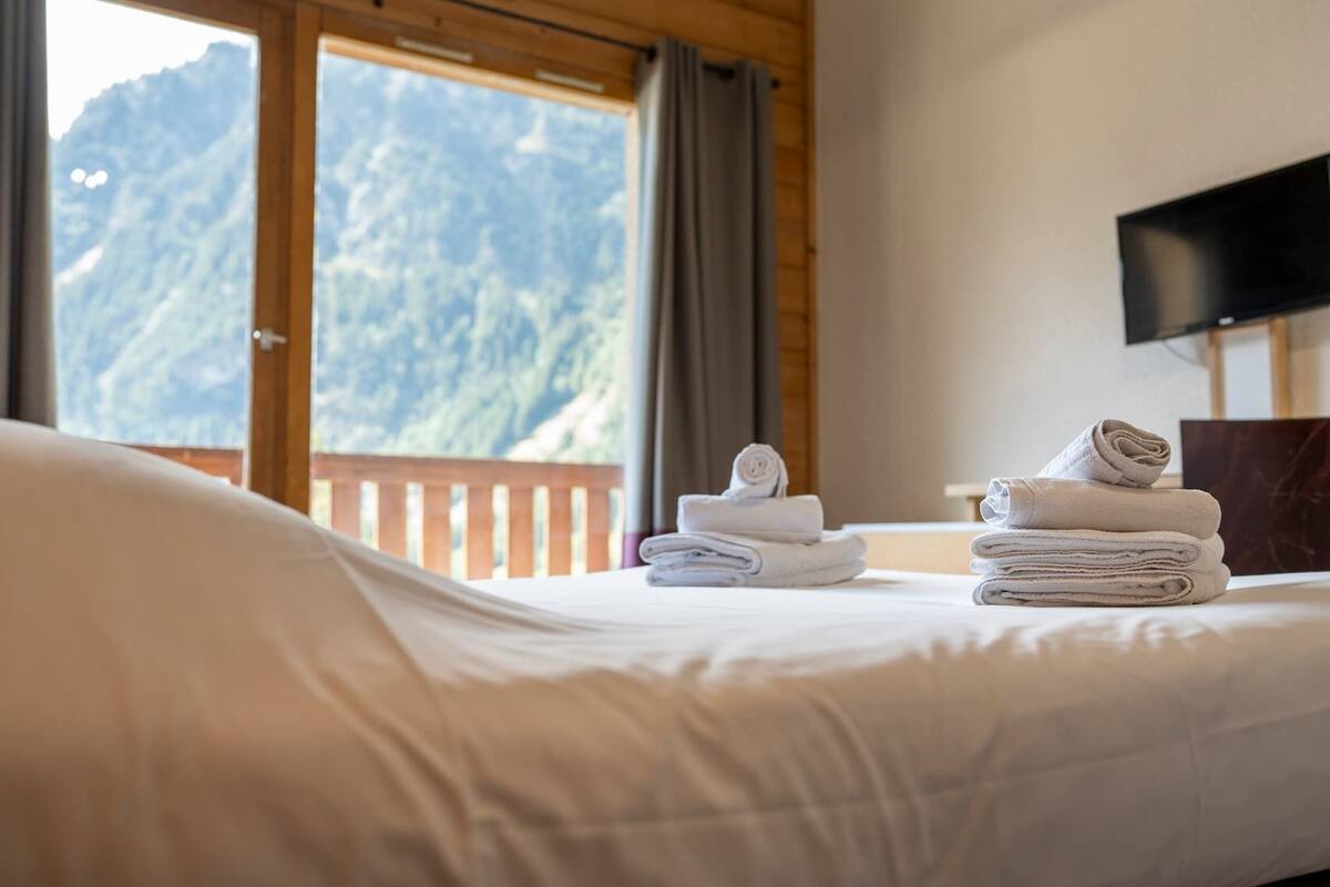 A hotel room with a bed, a mountain view, and a TV on the wall.