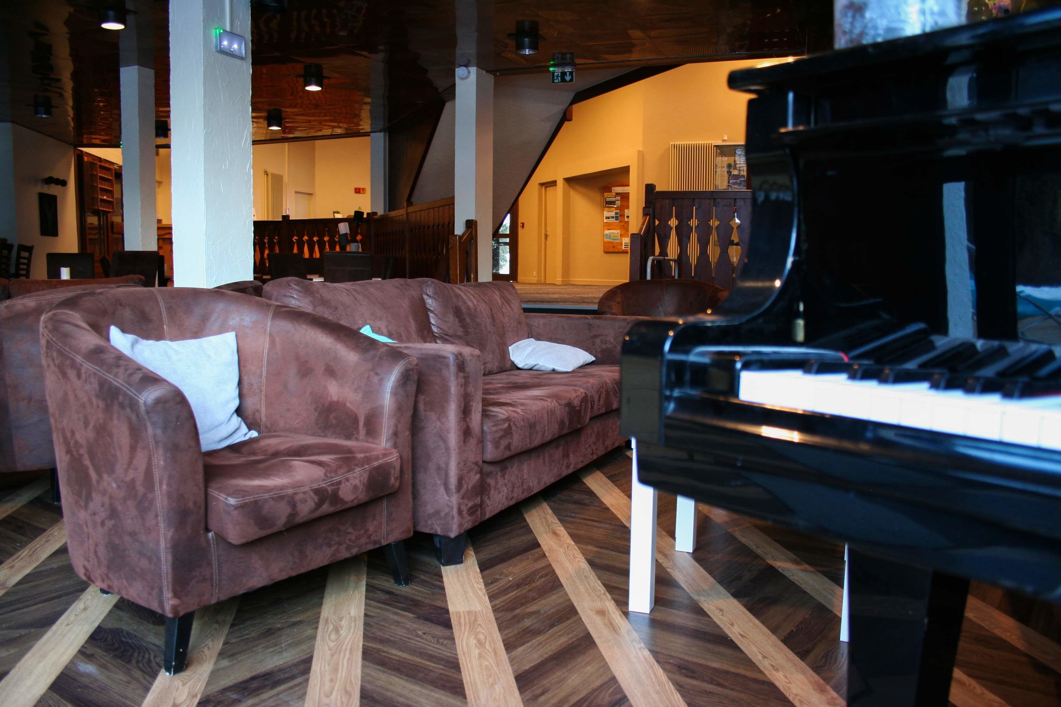 A room with a grand piano, brown leather sofas, and wooden parquet flooring.