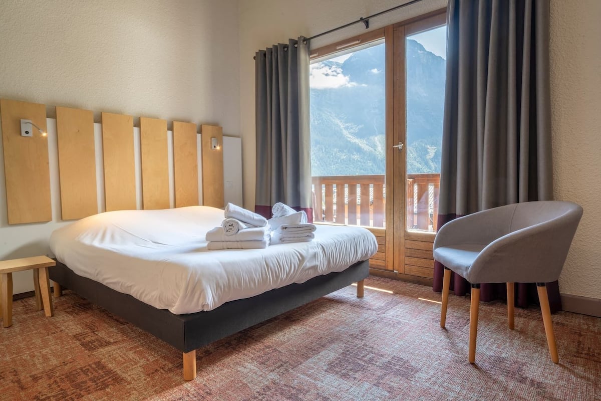 A hotel room with a bed, a chair, and a view of mountains through the window.