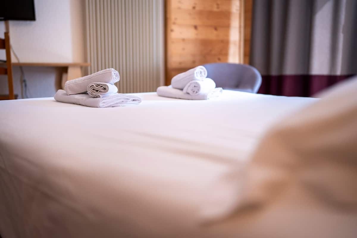 A neatly made bed with folded towels and a chair in a hotel room.