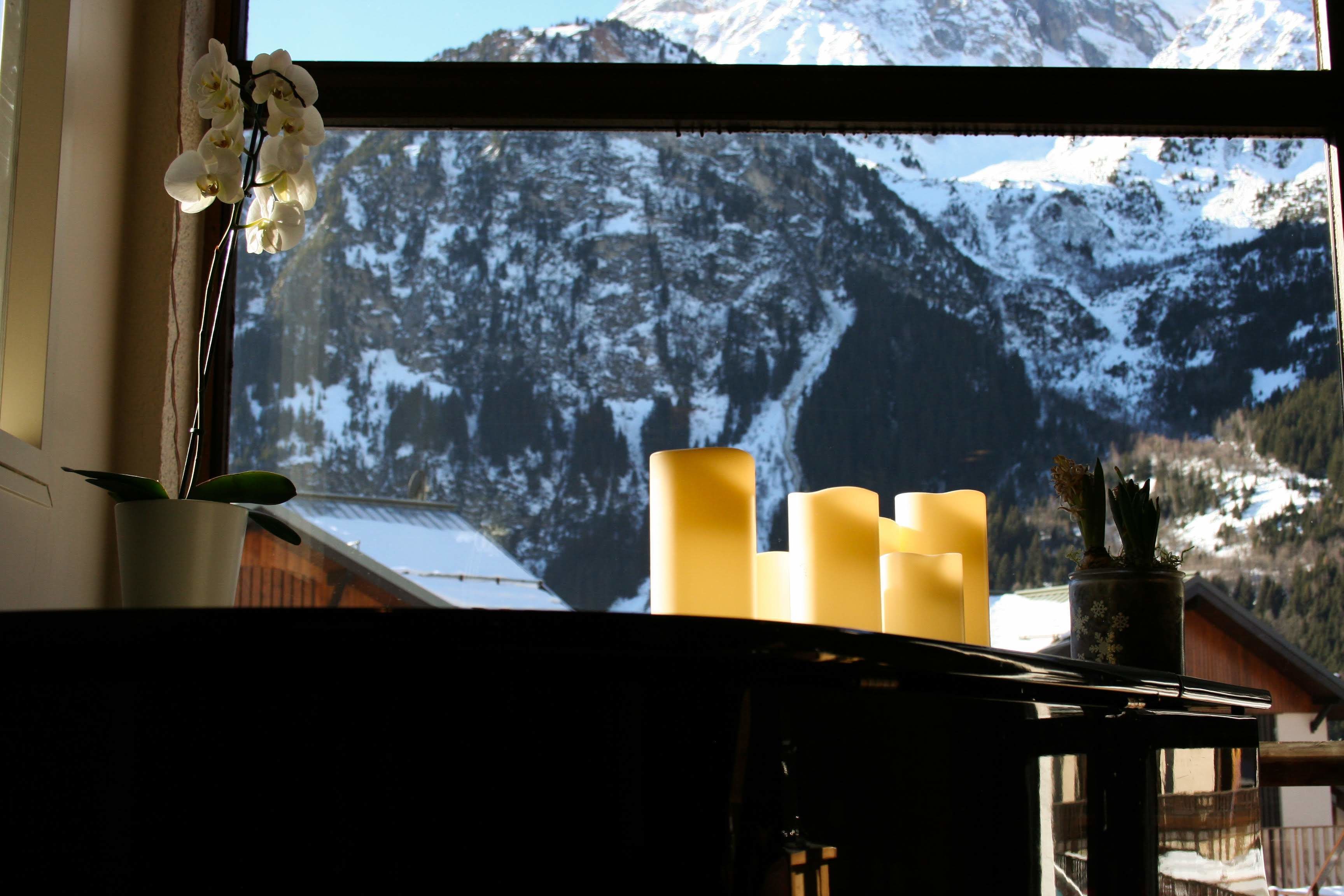 Una ventana con vistas a montañas nevadas, un candelabro con velas y una orquídea en maceta.